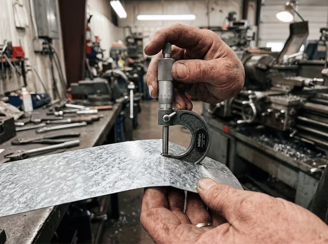 Micrometer measuring galvanized steel sheet thickness on workbench Micrometer measuring galvanized steel sheet thickness on workbench